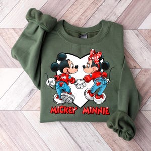 May include: Green sweatshirt with a white heart design featuring Mickey Mouse and Minnie Mouse holding hands. The text "Mickey Minnie" is printed below the heart.
