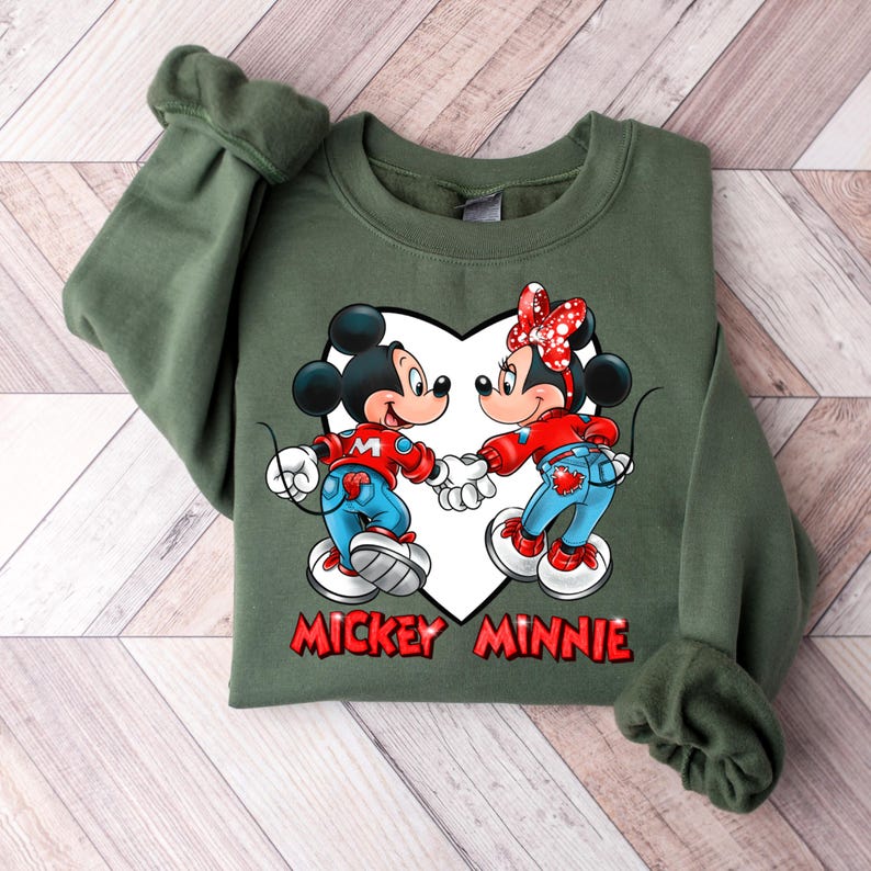 May include: Green sweatshirt with a white heart design featuring Mickey Mouse and Minnie Mouse holding hands. The text "Mickey Minnie" is printed below the heart.