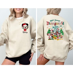 Op de afbeelding: Beige sweatshirt met een Mickey Mouse-afbeelding met een kerstmuts en het woord "Daddy" eronder. De achterkant heeft een kleurrijke Disney World-afbeelding met de tekst "Walt Disney's Disneyworld 1971".