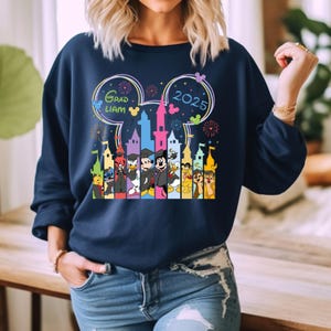 Puede incluir: Una sudadera azul marino con un gr&aacute;fico de Mickey Mouse y otros personajes de Disney frente al Castillo de Cenicienta. El gr&aacute;fico tambi&eacute;n incluye el texto "Grad Liam 2025" y fuegos artificiales.