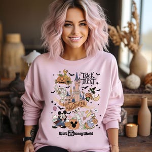 May include: Pink sweatshirt with a graphic print of Mickey Mouse, Goofy, and other Disney characters dressed in Halloween costumes. The graphic also includes a castle, pumpkins, bats, and candy. The text "Trick or Treat" and "2024 Halloween" are included in the graphic. The text "Walt Disney World" is at the bottom of the graphic.