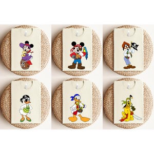 May include: Six cream-colored t-shirts featuring cartoon pirate characters. Designs include Mickey Mouse, Minnie Mouse, Donald Duck, Goofy, and other Disney characters. Each shirt is displayed on a round, woven placemat.