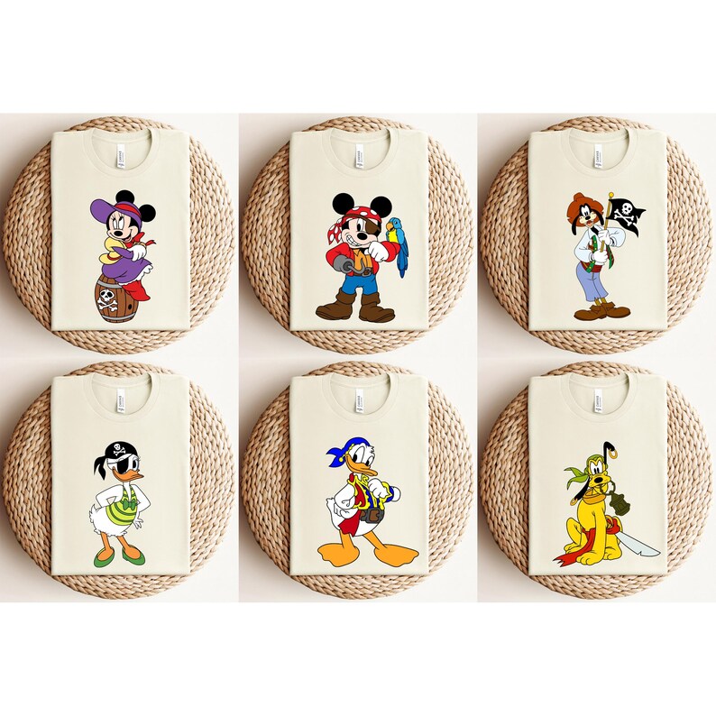 May include: Six cream-colored t-shirts featuring cartoon pirate characters. Designs include Mickey Mouse, Minnie Mouse, Donald Duck, Goofy, and other Disney characters. Each shirt is displayed on a round, woven placemat.