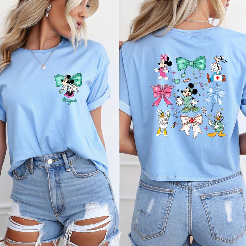 May include: Light blue t-shirt featuring a Minnie Mouse and Mickey Mouse graphic with a teal bow and the name "Megan". The back of the shirt has various Disney character graphics and bows. The shirt has rolled-up sleeves.
