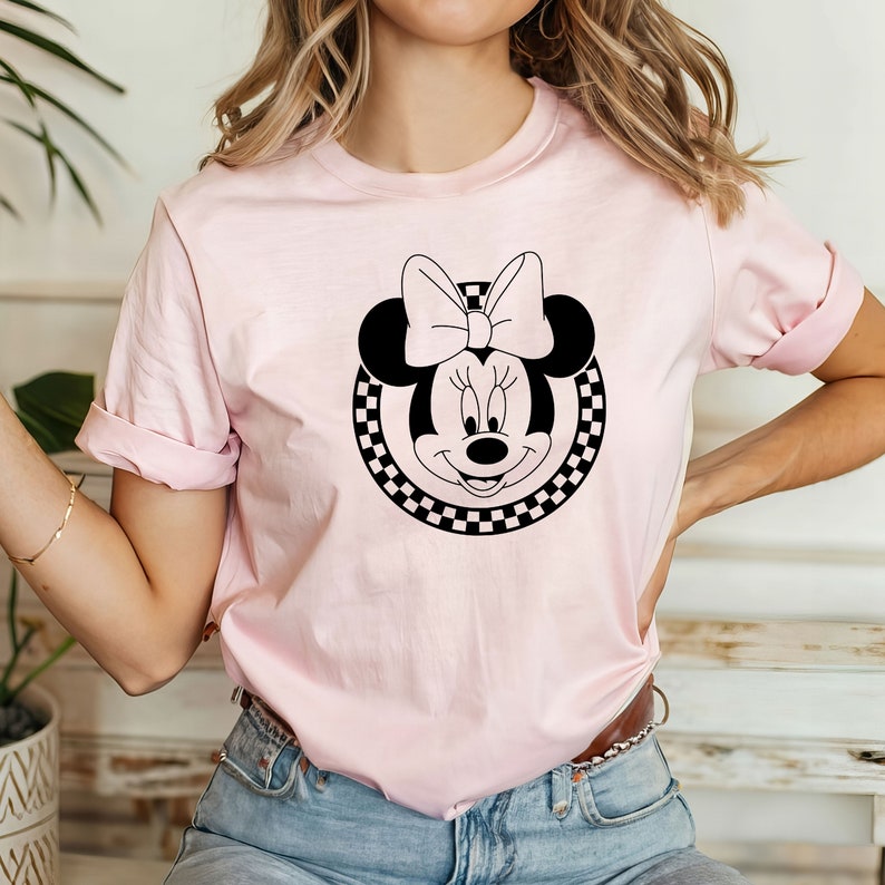 May include: A pink t-shirt featuring a black and white checkered circle surrounding a black and white image of Minnie Mouse with a large bow.