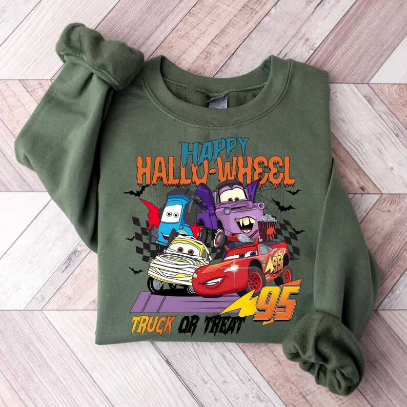 Może przedstawiać: Zielona bluza z nadrukiem kresk&oacute;wek samochod&oacute;w przebranych na Halloween. Tekst głosi "Happy Hallo-Wheel Truck or Treat".