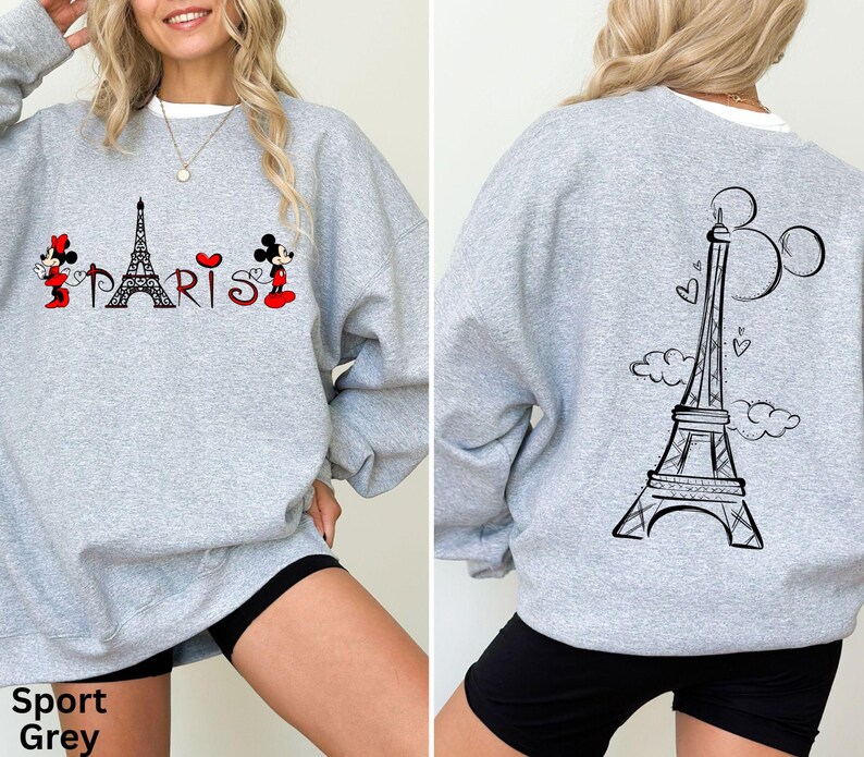 K&ouml;nnte beinhalten: Hellgraues Sweatshirt mit einem Front-Design, das den Eiffelturm, das Wort "PARIS" und Zeichentrickfiguren zeigt. Die R&uuml;ckseite des Sweatshirts hat ein schwarzes Eiffelturm-Design mit Herzen und Wolken. Der Text "Sport Grey" steht unten.