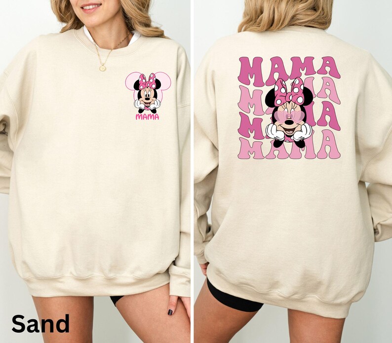 Puede incluir: Sudadera color arena con un gr&aacute;fico de Minnie Mouse, lazo rosa y la palabra "MAMA". La parte trasera presenta un gr&aacute;fico de Minnie Mouse m&aacute;s grande y la palabra "MAMA" en rosa, con fuente ondulada. Un estilo casual y c&oacute;modo.