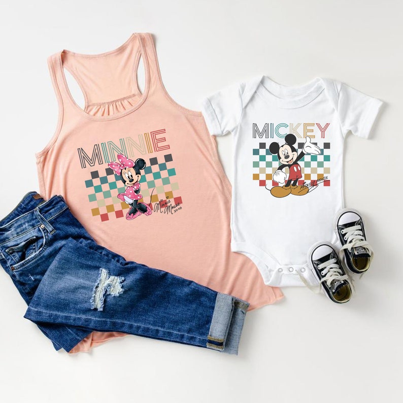 May include: A pink tank top with a retro checkered pattern and the text "MINNIE" in rainbow colors. A white bodysuit with the text "MICKEY" in rainbow colors and a retro checkered pattern. Both shirts feature a cartoon image of Minnie and Mickey Mouse.