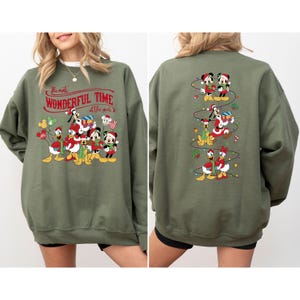 May include: Olive green sweatshirt featuring a festive graphic of Disney characters, including Mickey and Minnie Mouse, Donald and Daisy Duck, and Goofy, in holiday attire. The front of the sweatshirt has the text "The Most Wonderful Time of the Year".