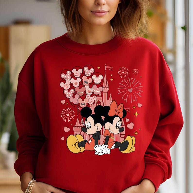 May include: Red sweatshirt with a graphic of Mickey and Minnie Mouse in front of Cinderella's Castle with balloons and fireworks. The text on the balloons says "LOVE" and "XOXO".