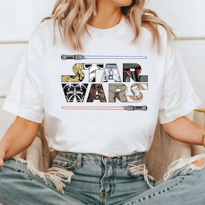 May include: White t-shirt with a graphic of the Star Wars logo. The logo is made up of images of characters from the Star Wars franchise, including Darth Vader, Yoda, and R2-D2.
