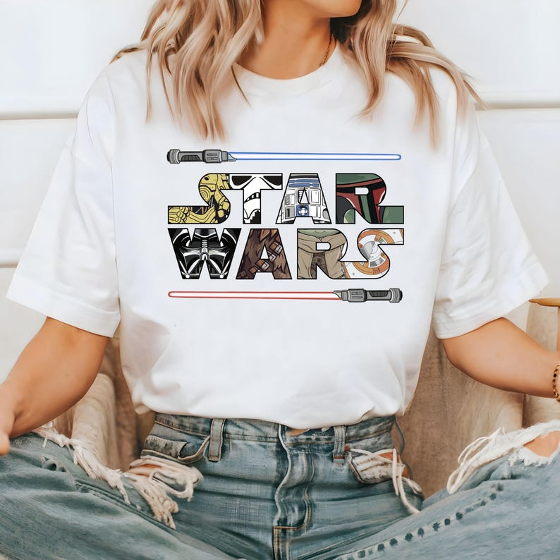 May include: White t-shirt with a graphic of the Star Wars logo. The logo is made up of images of characters from the Star Wars franchise, including Darth Vader, Yoda, and R2-D2.