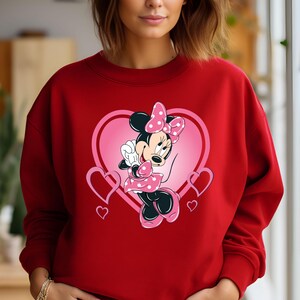 May include: Red sweatshirt with a pink heart and Minnie Mouse graphic. Minnie Mouse is wearing a pink polka dot bow and a pink dress with white polka dots.