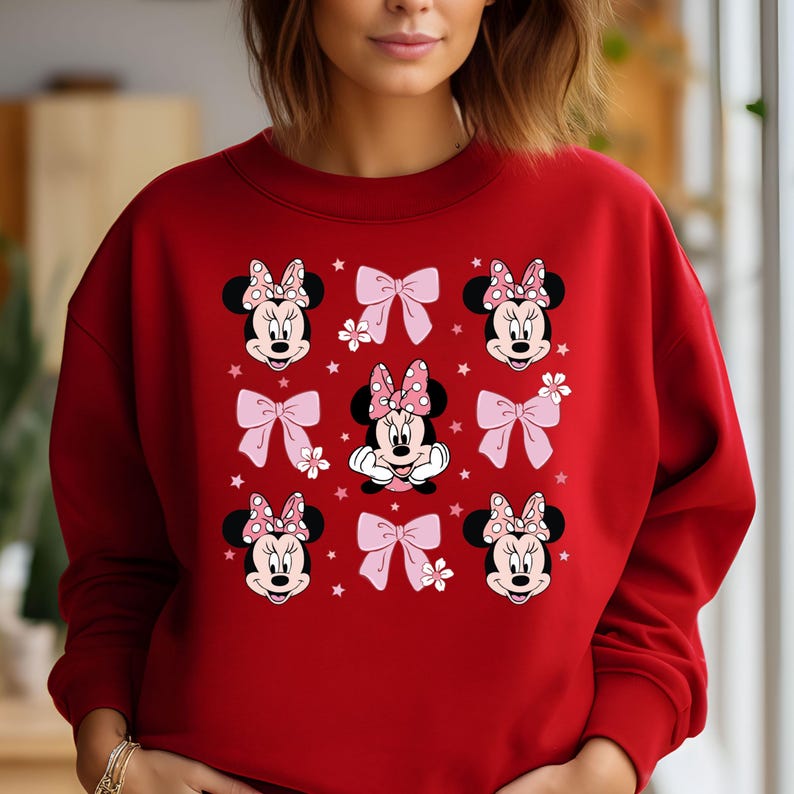 May include: Red sweatshirt with a pattern of Minnie Mouse faces and pink bows. The Minnie Mouse faces are wearing red polka dot bows.