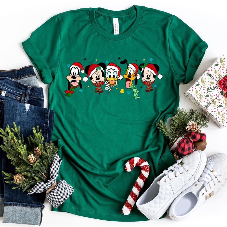 May include: Green t-shirt with a Christmas-themed design featuring Mickey Mouse, Minnie Mouse, Donald Duck, Goofy, and Pluto wearing Santa hats and scarves.