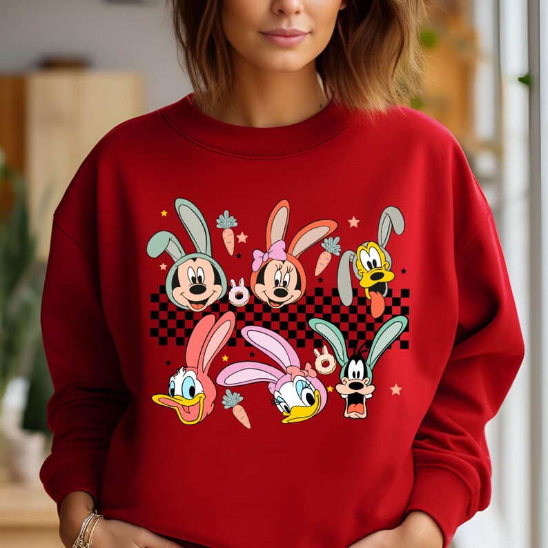 May include: Red sweatshirt with a graphic print of Disney characters dressed as bunnies. The characters include Mickey Mouse, Minnie Mouse, Donald Duck, and Goofy. The graphic is set against a checkered background with carrots and stars.
