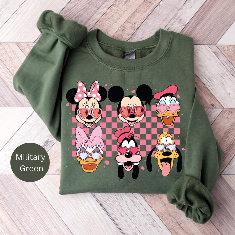 May include: A green sweatshirt with a checkered pattern and a print of Mickey Mouse, Minnie Mouse, Donald Duck, Goofy, and Pluto wearing heart-shaped sunglasses. The characters are in a row, with Mickey Mouse in the center.
