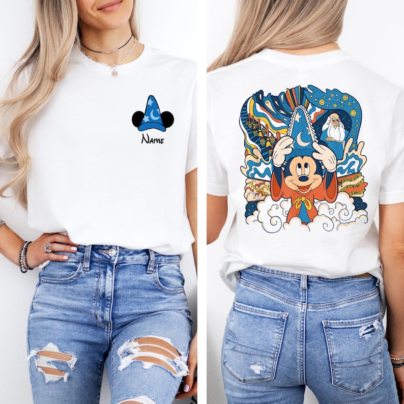 May include: White t-shirt with a blue Mickey Mouse sorcerer hat and the word "Name" printed on the front. The back of the shirt features a colorful illustration of Mickey Mouse as a sorcerer with a blue hat and a red robe, surrounded by clouds and stars.