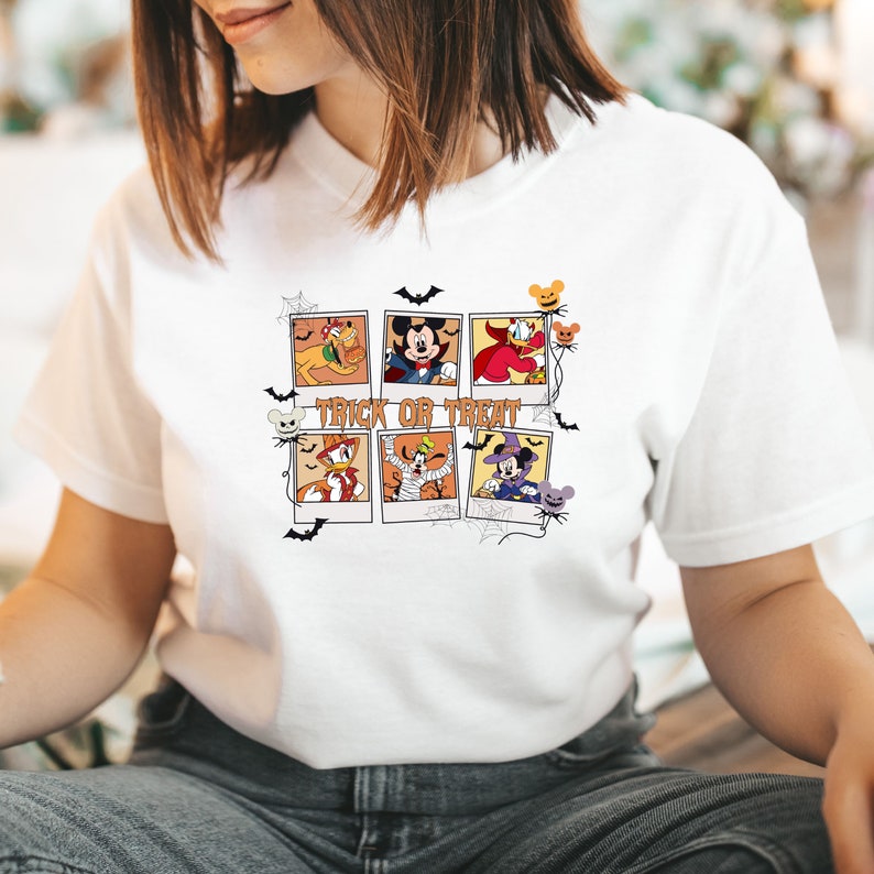 Op de afbeelding: Wit T-shirt met een grafische print van Mickey Mouse en zijn vrienden verkleed in Halloween-kostuums. De afbeelding bevat de tekst "Trick or Treat".