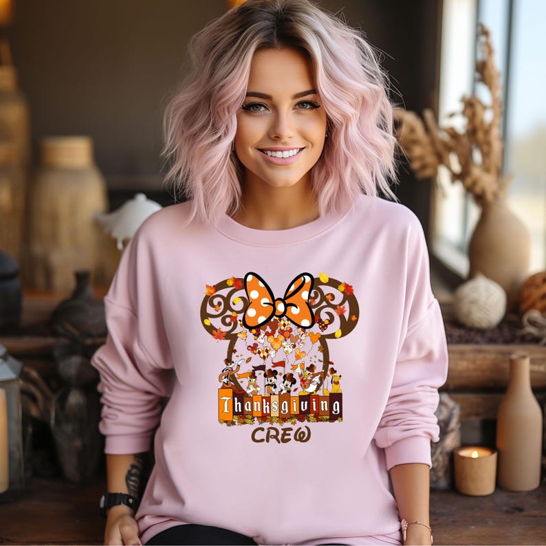 Puede incluir: Sudadera rosa claro con un dise&ntilde;o inspirado en Minnie Mouse, con un lazo de lunares y hojas de oto&ntilde;o. El gr&aacute;fico incluye el texto "Thanksgiving Crew" y varios personajes de dibujos animados, perfecto para la temporada festiva.