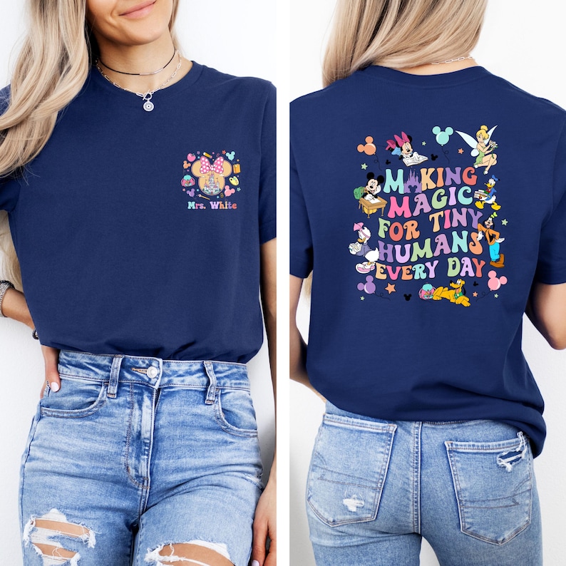 May include: Navy blue t-shirt with a colorful graphic on the front and back. The front features a Minnie Mouse design with the text "Mrs. White." The back displays the phrase "MAKING MAGIC FOR TINY HUMANS EVERY DAY" with Disney characters.