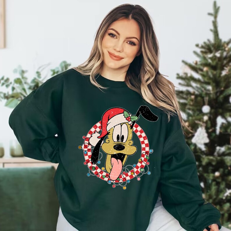 May include: A dark green sweatshirt with a Christmas-themed graphic of Pluto wearing a Santa hat and surrounded by a red and white checkered wreath with lights.