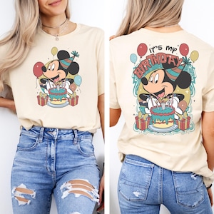 以下が含まれることがあります： ベージュのTシャツに、ミッキーマウスが誕生日ケーキとろうそくを持っているヴィンテージスタイルのグラフィックがプリントされています。Tシャツの後ろには「It's my Birthday」という文字がプリントされています。