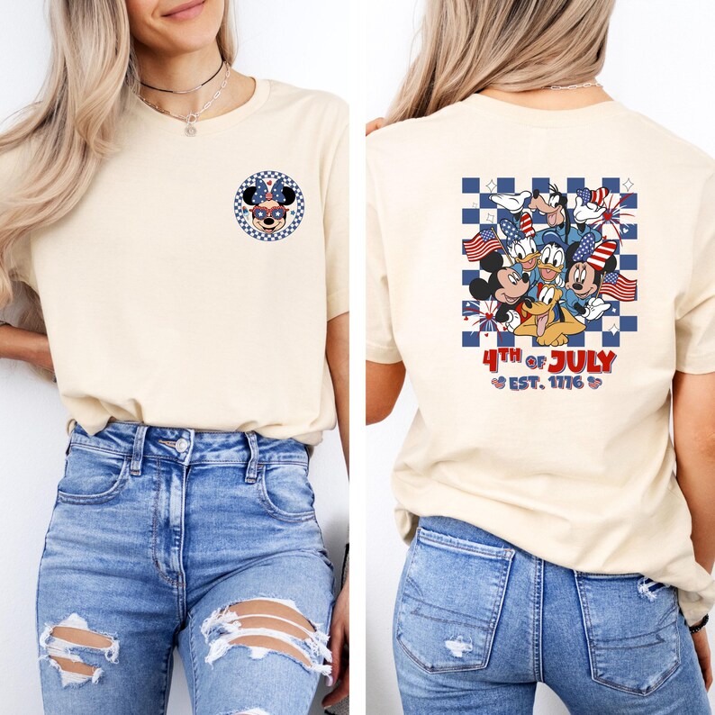 Puede incluir: Camiseta color crema con un dise&ntilde;o de Minnie Mouse en la parte delantera y un grupo de personajes de Disney con banderas americanas en la parte trasera. La parte trasera de la camiseta tambi&eacute;n tiene el texto "4th of July Est. 1776."
