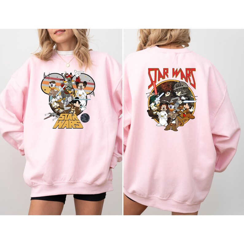 May include: Pink sweatshirt featuring a graphic of Disney characters in a Star Wars theme. The front design includes Mickey Mouse, Donald Duck, and other characters. The back of the sweatshirt has a similar design with the words "Star Wars" in red.