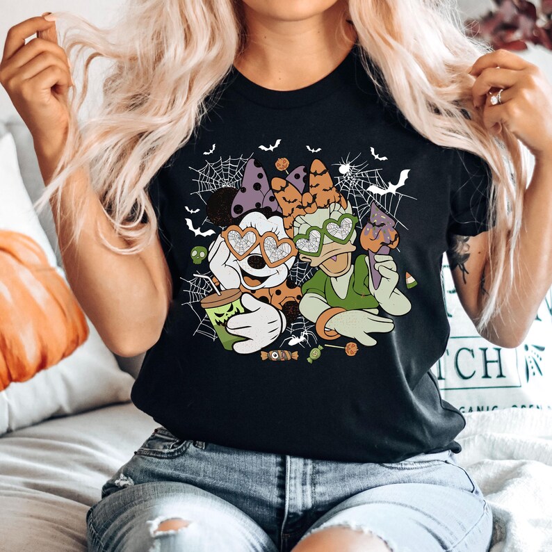 May include: Black t-shirt with a graphic print of Mickey Mouse and Donald Duck wearing heart-shaped sunglasses. The graphic also includes bats, spiderwebs, and candy. The text "Boo!" is printed on the shirt.