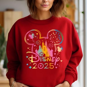 May include: Red sweatshirt with a rainbow-colored Mickey Mouse silhouette, a castle, and fireworks. The text "DISNEY 2025" is below the silhouette.