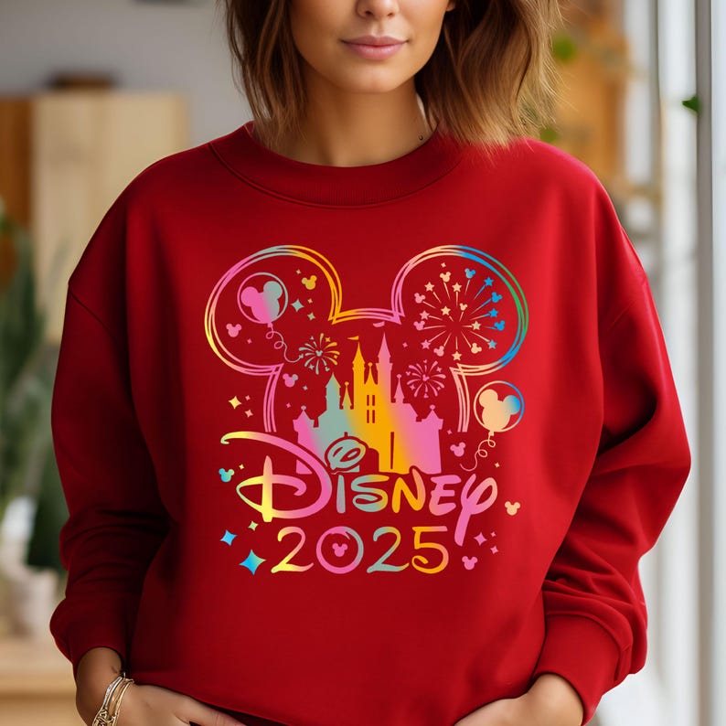 May include: Red sweatshirt with a rainbow-colored Mickey Mouse silhouette, a castle, and fireworks. The text "DISNEY 2025" is below the silhouette.