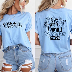 May include: Light blue t-shirt featuring a black graphic of Disney characters on the front and back. The front graphic includes Minnie Mouse, Mickey Mouse, and Pluto. The back graphic says "Family Vacation 2026."