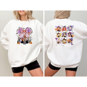 May include: White sweatshirt featuring a Halloween-themed graphic on the front and back. The front design includes a large bow, bats, and characters. The back displays nine framed images of characters with witch hats and balloons. A festive and fun design.
