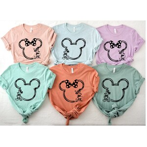 May include: Six t-shirts with a black and white outline of Mickey Mouse's head with Minnie Mouse standing inside. The shirts are in various colors: light pink, light blue, lavender, light green, peach, and dark green.