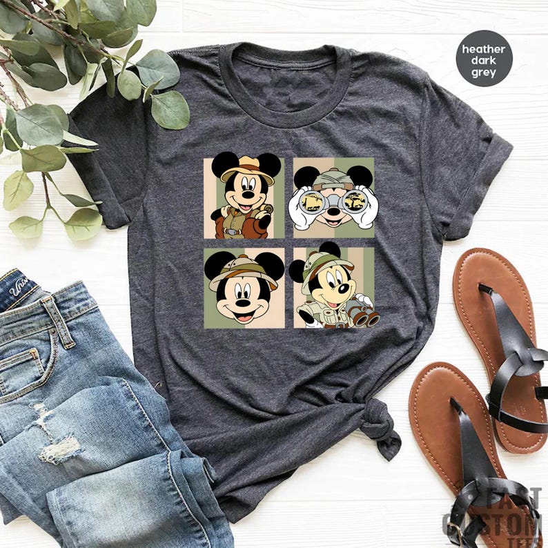 K&ouml;nnte beinhalten: Dunkelgraues T-Shirt mit einem viergeteilten Motiv von Mickey Mouse in Safari-Kleidung. Jedes Feld zeigt Mickey in verschiedenen Posen, mit Hut und Fernglas. Der Text "heather dark grey" befindet sich oben rechts.