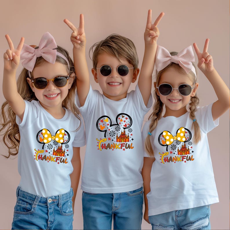 Puede incluir: Tres ni&ntilde;os con camisetas blancas con un gr&aacute;fico colorido de orejas de Mickey Mouse, un lazo y la palabra "THANKFUL". Los ni&ntilde;os llevan gafas de sol y hacen signos de paz.