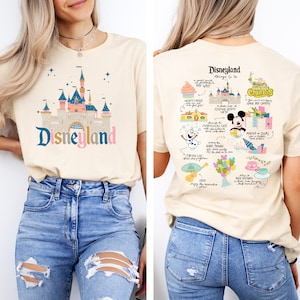 May include: A beige t-shirt with a graphic of the Disneyland castle on the front and a list of things to do at Disneyland on the back. The text on the back includes "Disneyland", "Things to Do", "Mickey's House", "Sleeping Beauty", "Jungle Cruise", "Haunted Mansion", "Peter Pan", "It's a Small World", "Coco", "Mad Tea Party", "Churros", "Storytellers Cafe", "Minnie & Daisy", "Pixie Hollow", "Night Parade", "The Disneyland Railroad", "and more!"