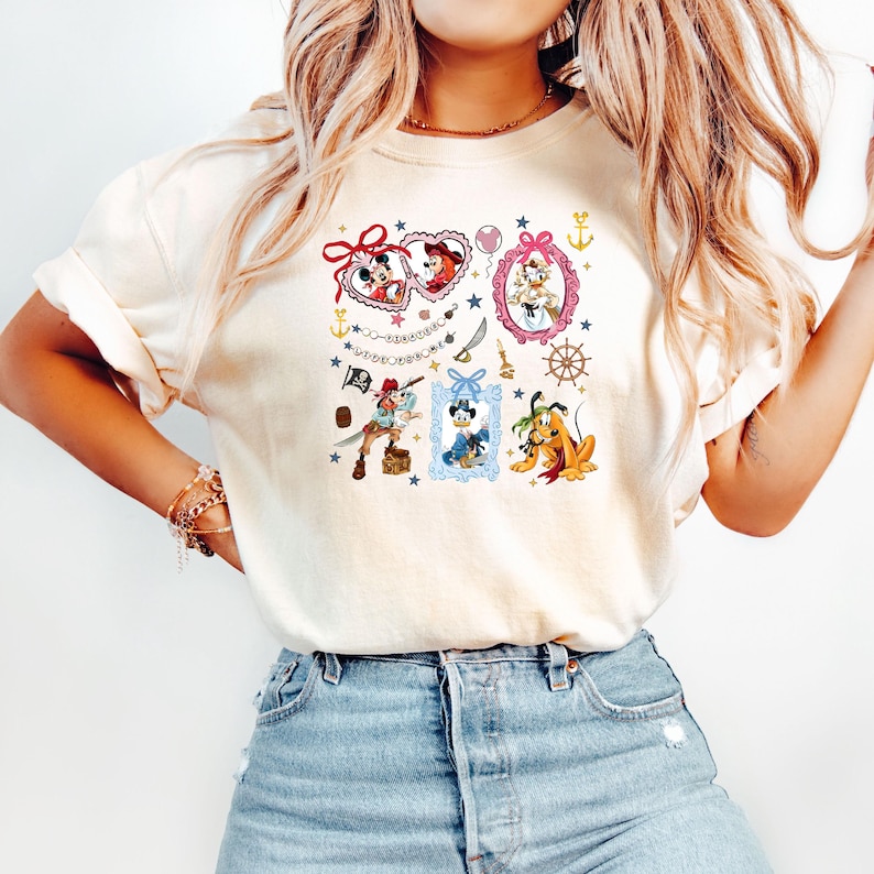May include: A white t-shirt with a colorful graphic print featuring various Disney characters, including Mickey Mouse, Minnie Mouse, Donald Duck, Goofy, and Pluto. The graphic includes hearts, stars, anchors, and other nautical elements. The text "Wishes Do Come True" is included in the graphic.