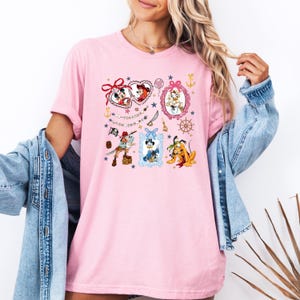 May include: Pink t-shirt with a graphic print of various Disney characters in frames. The characters include Mickey Mouse, Minnie Mouse, Donald Duck, Goofy, and Pluto. The text on the shirt reads "To conquer the world, you need a good crew".