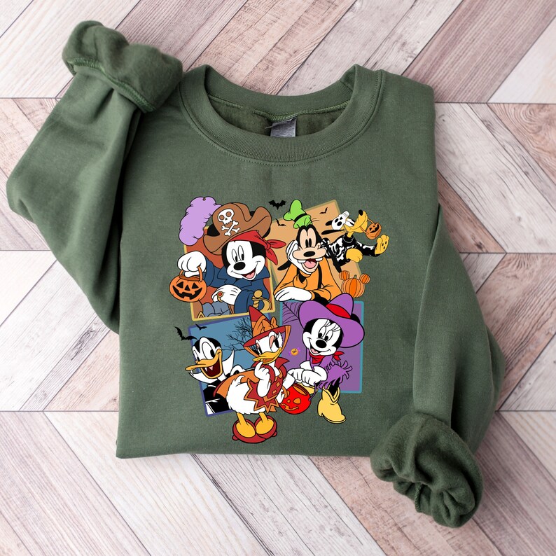 May include: Green sweatshirt with a colorful print of Mickey Mouse, Minnie Mouse, Donald Duck, Goofy, and Pluto dressed in Halloween costumes. The characters are holding pumpkins and candy.