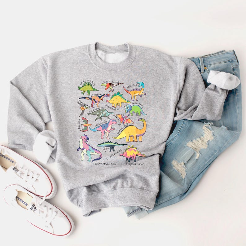 May include: A gray sweatshirt with a colorful dinosaur print. The dinosaurs are arranged in a circle and labeled with their names. The sweatshirt is a comfortable and stylish way to show your love for dinosaurs.