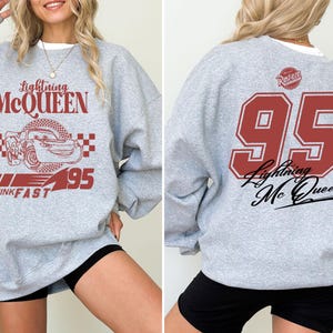 May include: Gray sweatshirt with a red and black graphic of Lightning McQueen from the Cars movie. The graphic includes the text "Lightning McQueen", "Think Fast", and "95". The back of the sweatshirt has a large red number "95" with the text "Lightning McQueen" underneath.