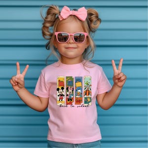 May include: A pink t-shirt featuring Mickey Mouse, Minnie Mouse, Donald Duck, and Goofy, with the words "back to school." The shirt is worn by a child wearing pink sunglasses and a pink bow.