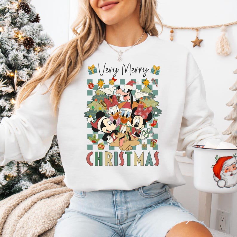 May include: White sweatshirt with a colorful graphic featuring Mickey Mouse, Minnie Mouse, Donald Duck, Goofy, and other Disney characters. The text "Very Merry Christmas" is displayed in green and red. The sweatshirt is a festive holiday design.