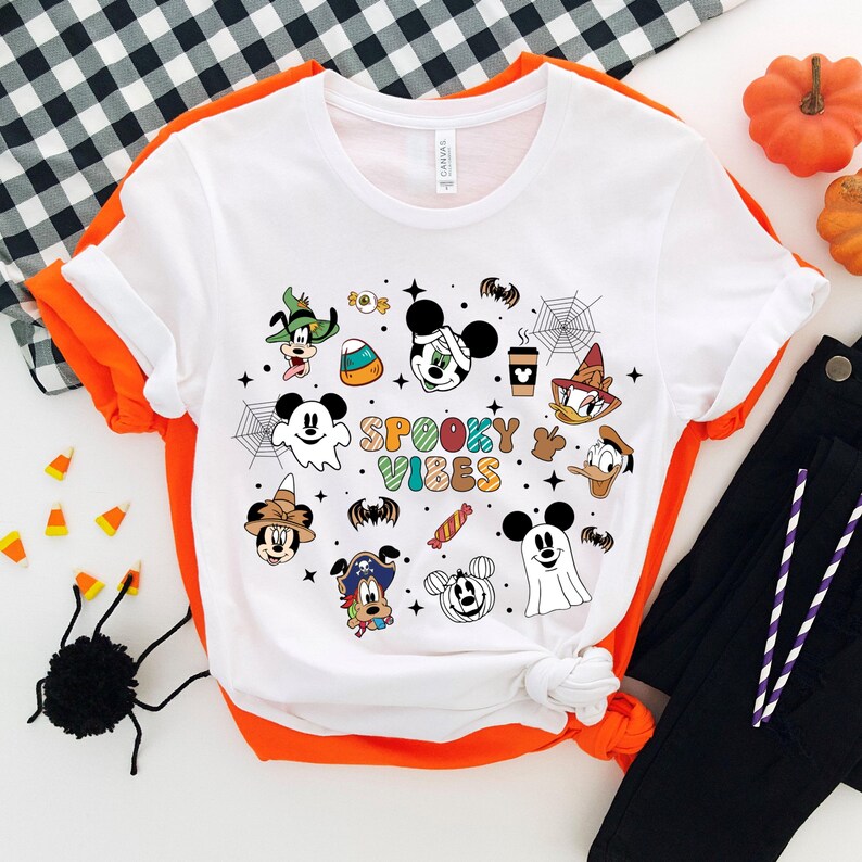 May include: White t-shirt featuring a colourful graphic of various Disney characters in Halloween costumes. The text "Spooky Vibes" is displayed in the centre of the design.