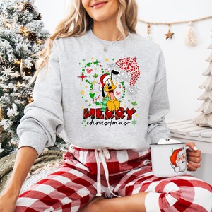 May include: A light gray sweatshirt with a Pluto graphic wearing a Santa hat and scarf, with the words "MERRY christmas" in a plaid design. The sweatshirt is paired with red and white plaid pajama pants.