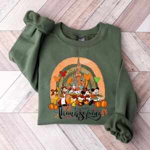 May include: Green sweatshirt featuring a Thanksgiving design with Disney characters, pumpkins, and a castle. The graphic includes the text "Happy Thanksgiving" in a script font, with fall leaves and Mickey Mouse balloons.