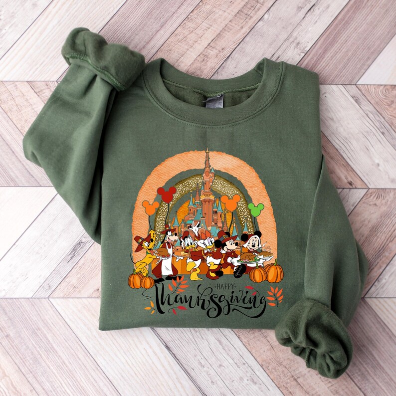 May include: Green sweatshirt featuring a Thanksgiving design with Disney characters, pumpkins, and a castle. The graphic includes the text "Happy Thanksgiving" in a script font, with fall leaves and Mickey Mouse balloons.